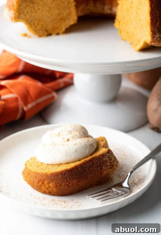 A delicious slice of sweet potato pound cake on a white plate, garnished with a dollop of whipped cream and a sprinkle of cinnamon, ready to be enjoyed.