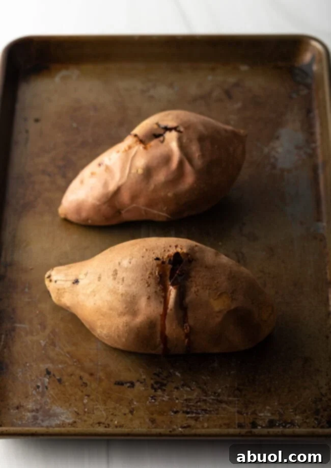 Two perfectly baked sweet potatoes cooling on a baking sheet, ready for mashing for the pound cake recipe.