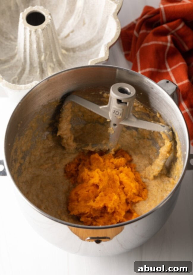 Rich cake batter with sweet potato mash being blended in a mixing bowl with a paddle attachment.