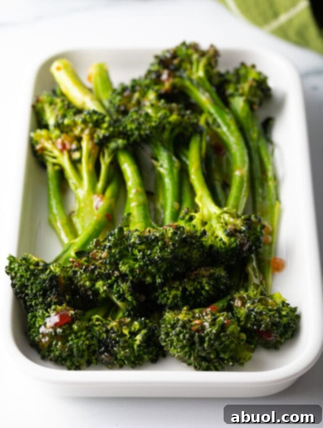 Roasted broccolini with sweet chili glaze stacked on a white rectangle serving platter.
