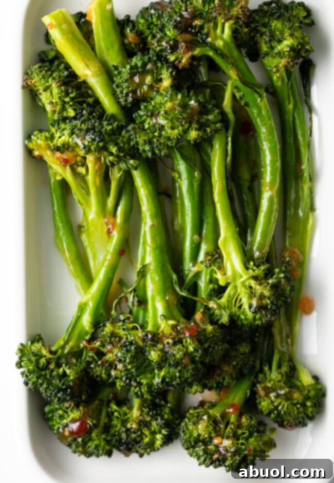 Roasted broccolini recipe finished - with sweet chili glaze stacked on a white rectangle serving platter.