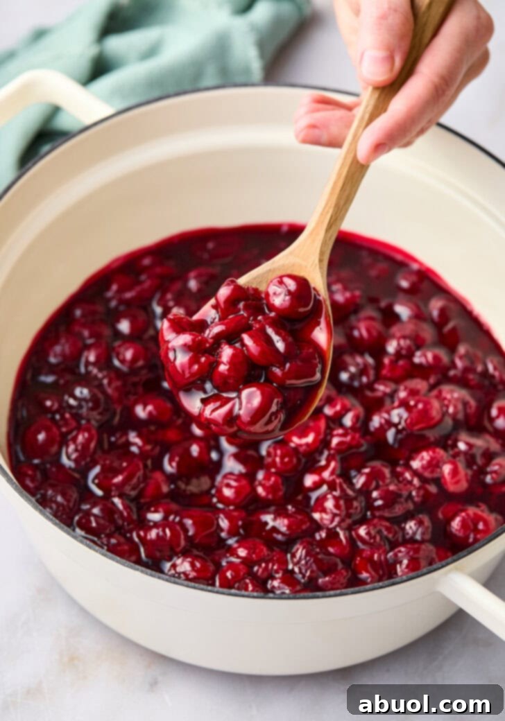 Cherry pie mixture in a large pot with a wooden spoon scooping some up. 