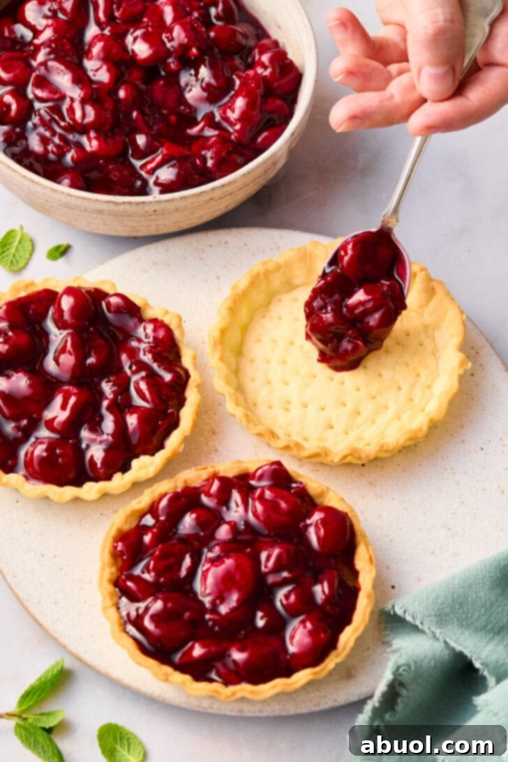 Filling mini cherry pie crusts with fruit filling.