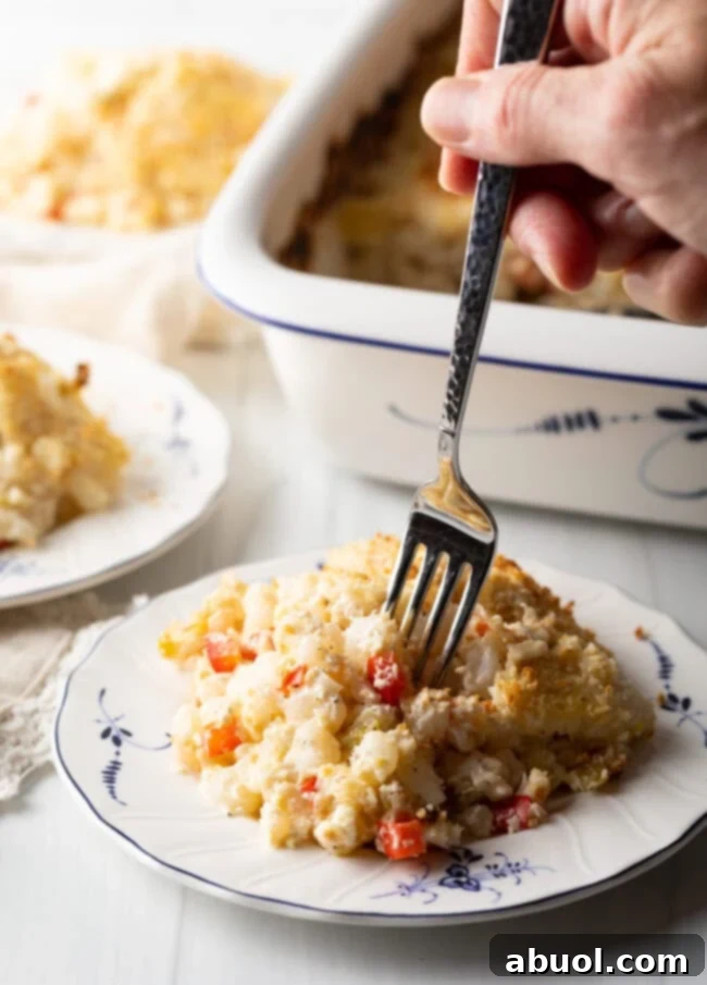 Golden Cheesy Hominy Bake 4 Hand with fork taking a bite from portion of cheesy hominy casserole.