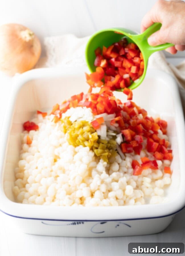 Golden Cheesy Hominy Bake 6 Hand pouring diced red peppers into casserole dish with other ingredients.