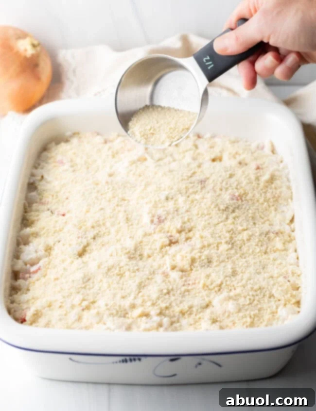 Golden Cheesy Hominy Bake 8 Hand pouring bread crumbs onto the top of the casserole.