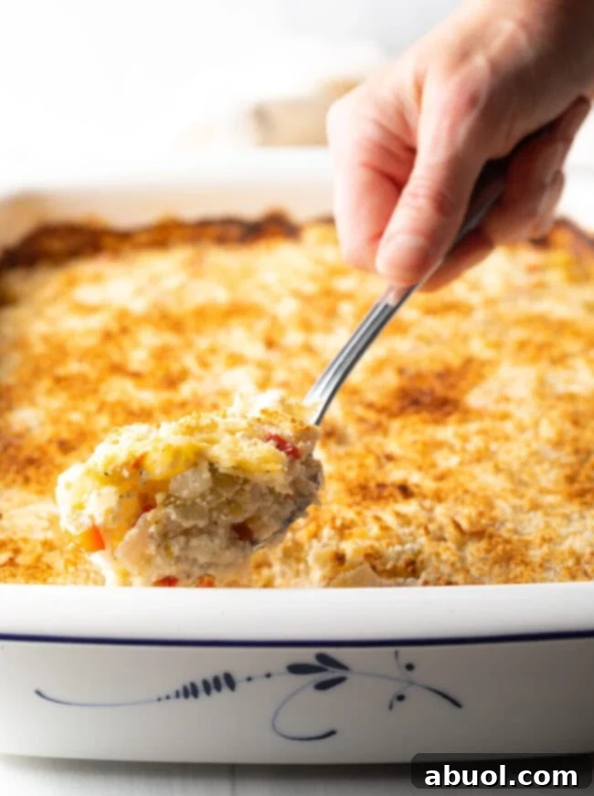 Golden Cheesy Hominy Bake 10 Hand with large metal spoon, scooping a portion from the casserole dish.