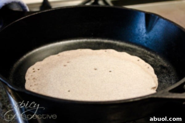 Injera bread batter being poured and expertly cooked in a skillet, visibly showing the formation of characteristic bubbles on its surface.