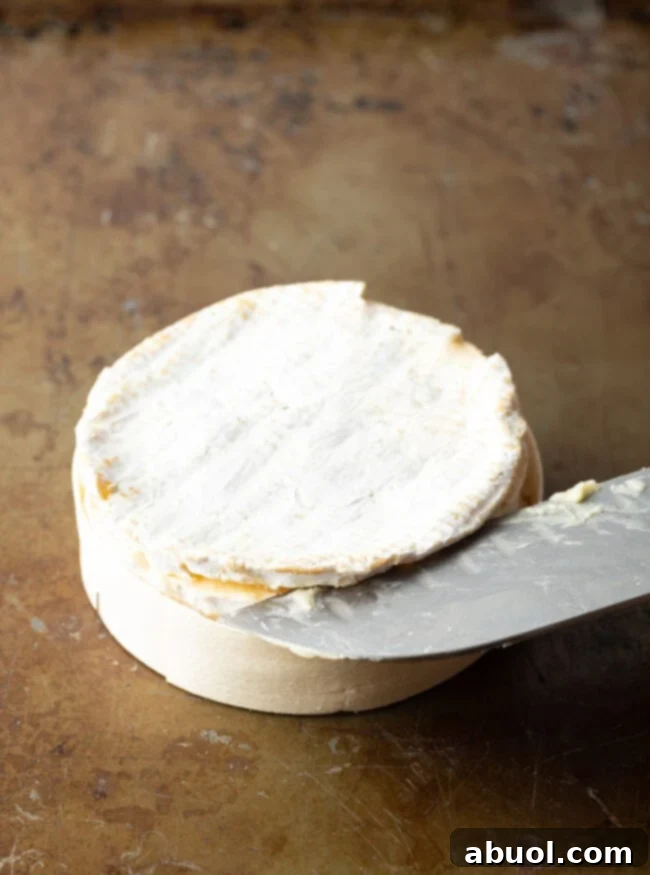 Sharp knife slicing through the top rind of the cheese.