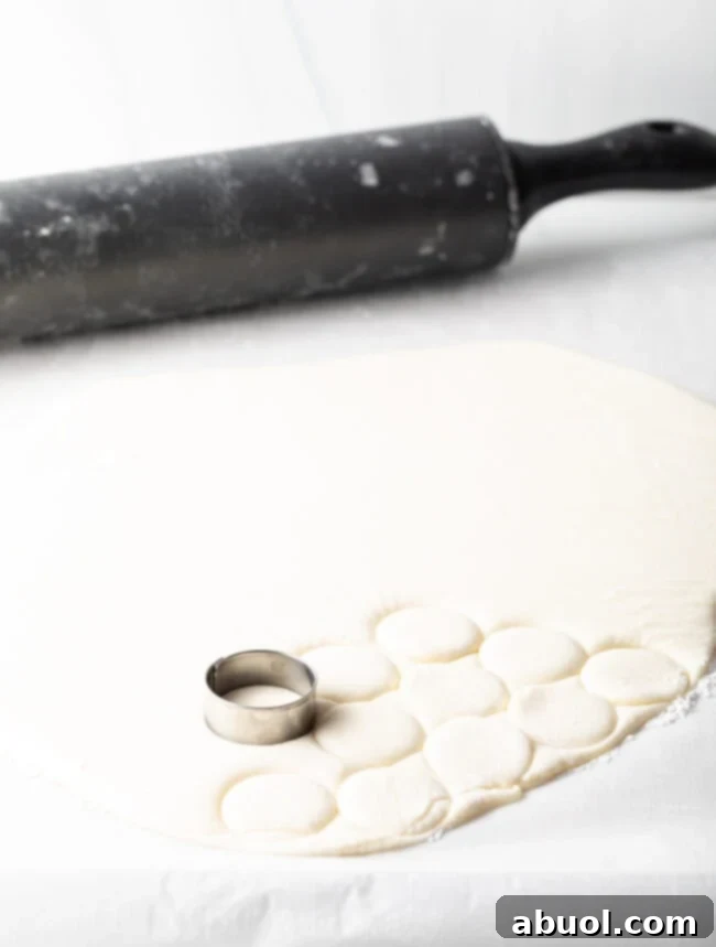 Patty dough rolled out in a sheet, 1-inch metal round cookie cutter making small circles.