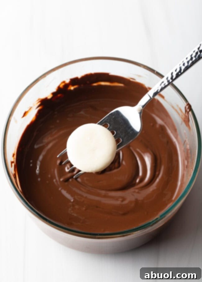Fork with white dough disc hovering above a glass bowl of melted chocolate.