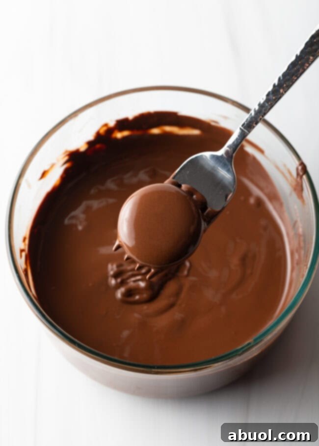 Fork with chocolate-coated candy, hovering above bowl of melted chocolate.