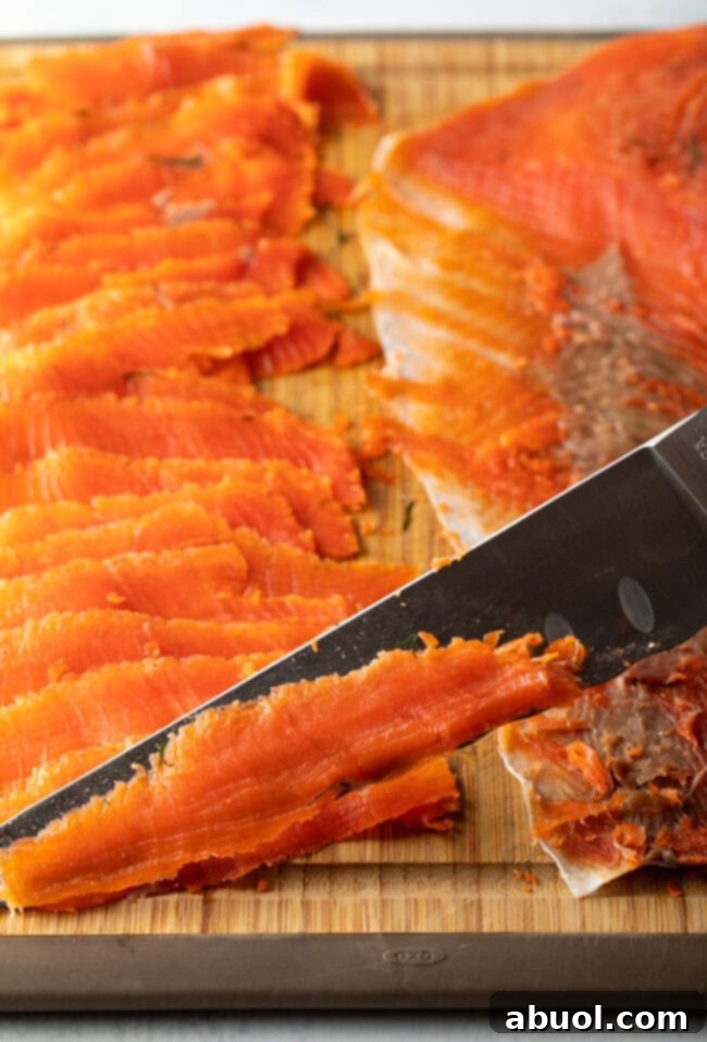 A close-up shot of a professional's sharp knife expertly carving thin, almost translucent slices of cured gravlax against the grain of the salmon.