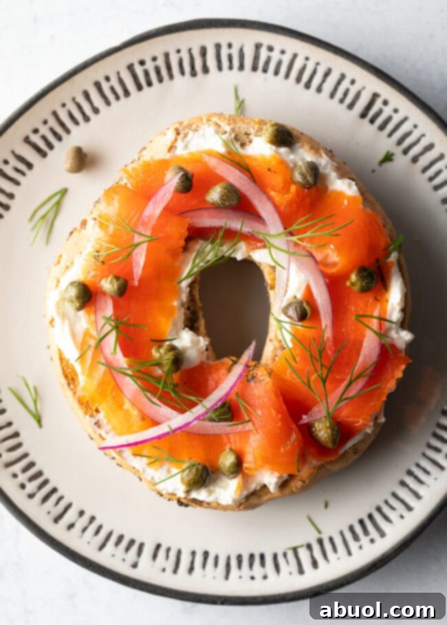 A top-down view of a delectable half bagel generously topped with smooth cream cheese, elegantly arranged slices of smoked gravlax, tangy capers, and delicate rings of sliced red onions, all ready to be enjoyed.