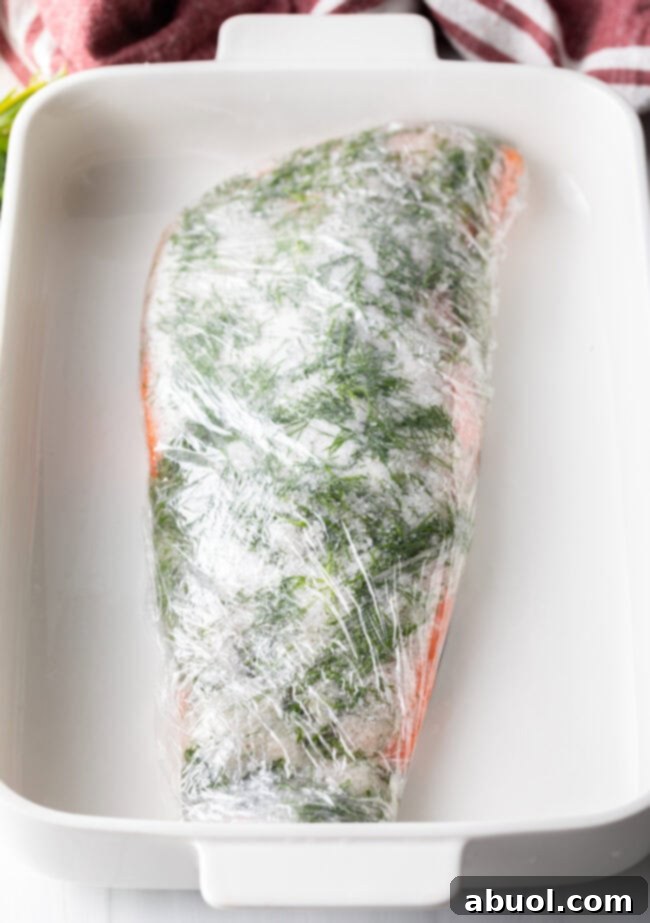 The salmon fillet, now thoroughly coated in the cure mixture, is meticulously wrapped in several layers of plastic wrap, preparing it for the pressing stage.