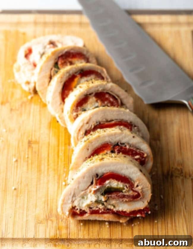 Stuffed chicken roulade, thin sliced on a cutting board with large knife.