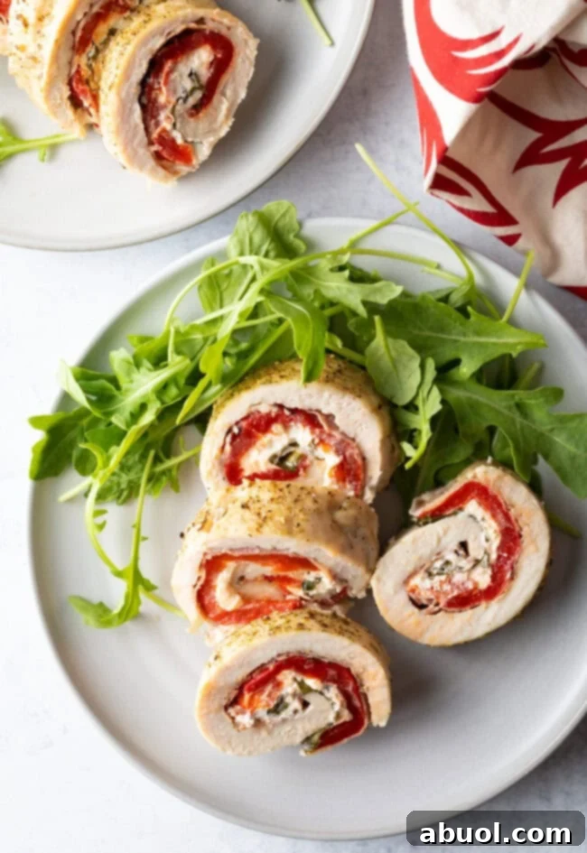 Top down view of slices of stuffed chicken roulade on a white plate with fresh arugula.