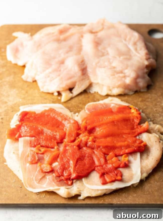 Slices of roasted red pepper laid flat on open slices of raw chicken. 