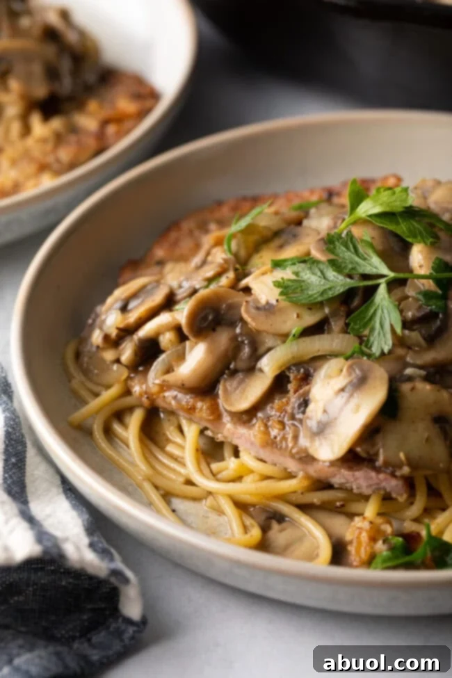 Close view final shot of veal scallopini recipe. There is a plate with pasta and  mushroom wine sauce, with fresh parsley.