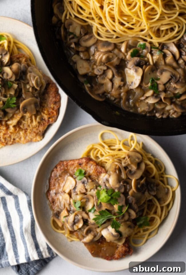 Top down view, skillet with pasta and mushroom sauce, two plates with servings from the veal scallopini recipe.