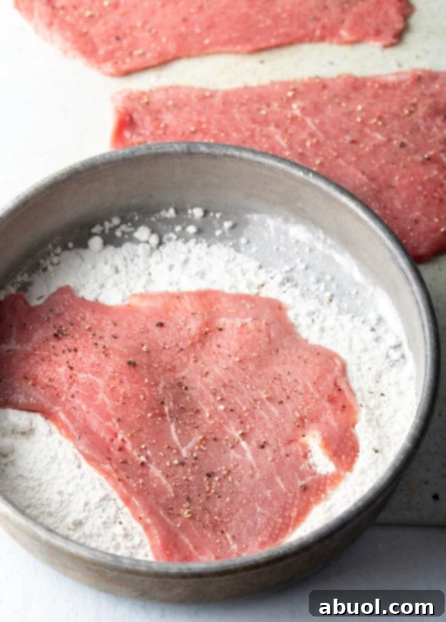 Raw cutlet in pan of flour.