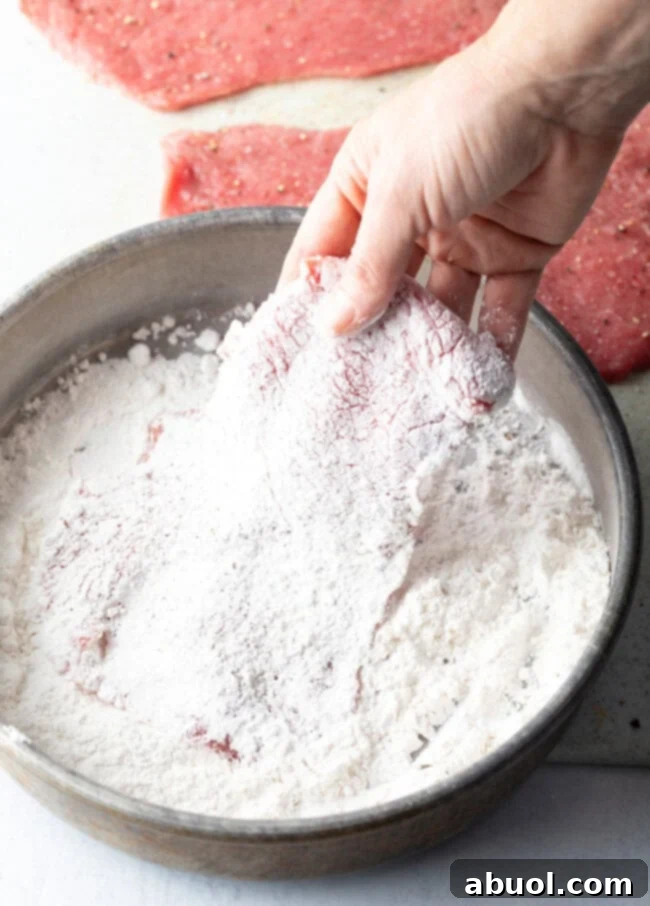 Hand dredging veal cutlet in flour.