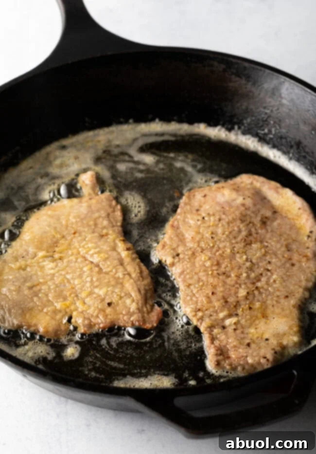 Two large flour cutlets frying in a cast iron skillet.