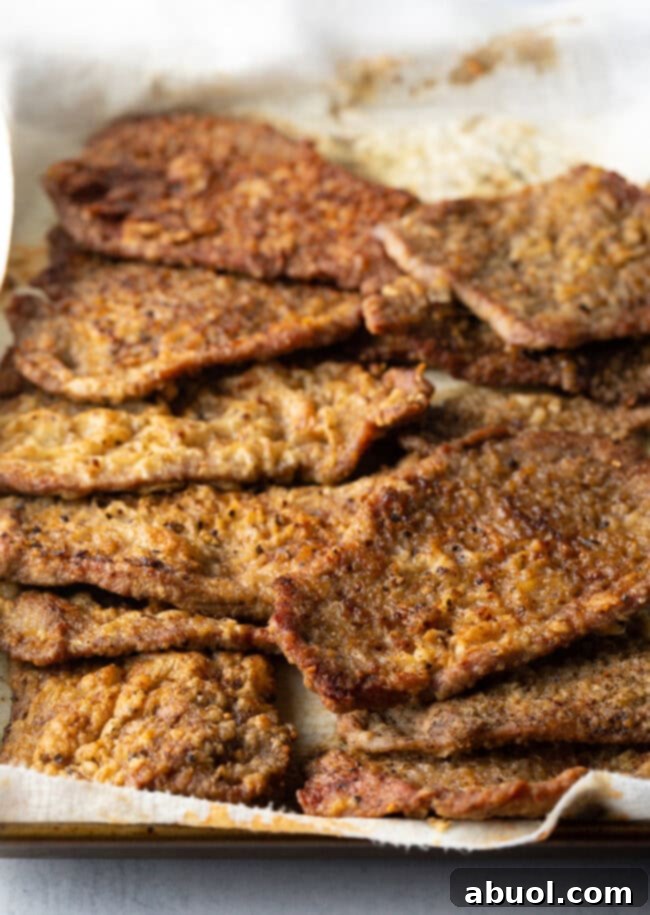 A dozen pan fried veal cutlets on paper towels.