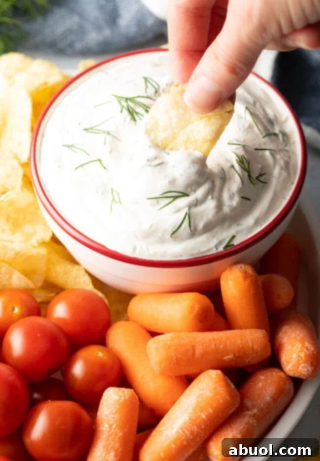 Hand dipping potato chip into bowl of creamy dill dip.