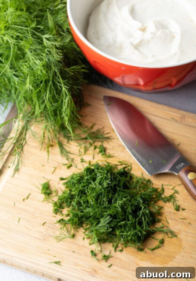 Fresh dill chopped on a wood cutting board with large knife.