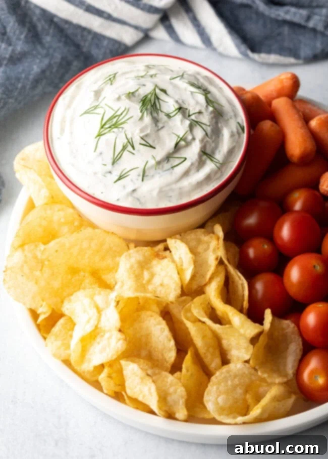 Creamy sour cream dip in a bowl, surrounded by potato chips, cherry tomatoes, and baby carrots.
