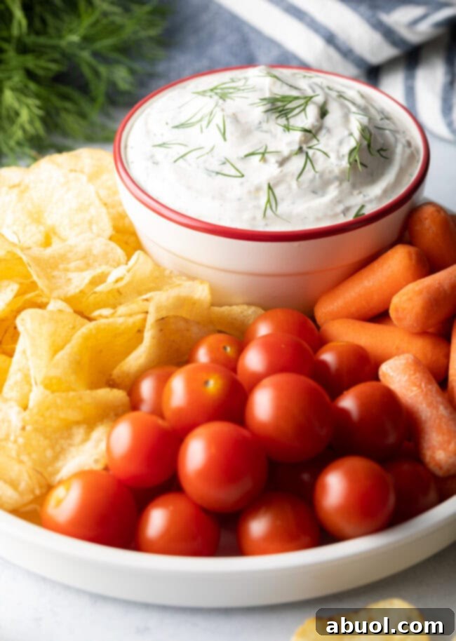 Dip in a bowl, surrounded by potato chips, cherry tomatoes, and baby carrots.