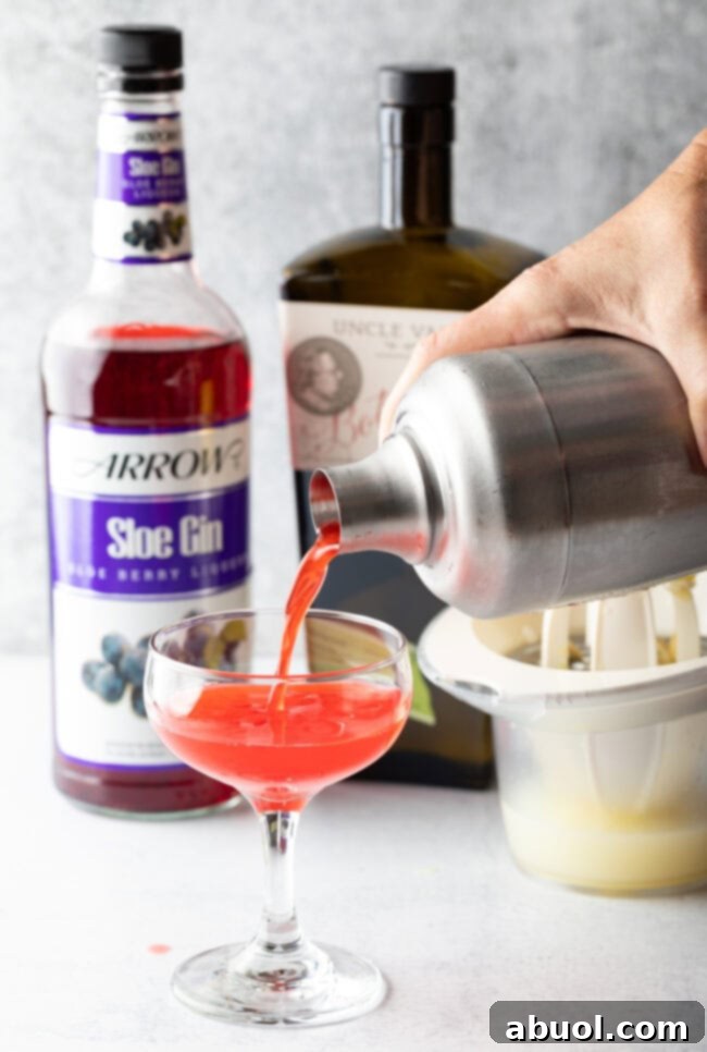 Hand pour pink liquid from metal cocktail shaker into martini style glass.