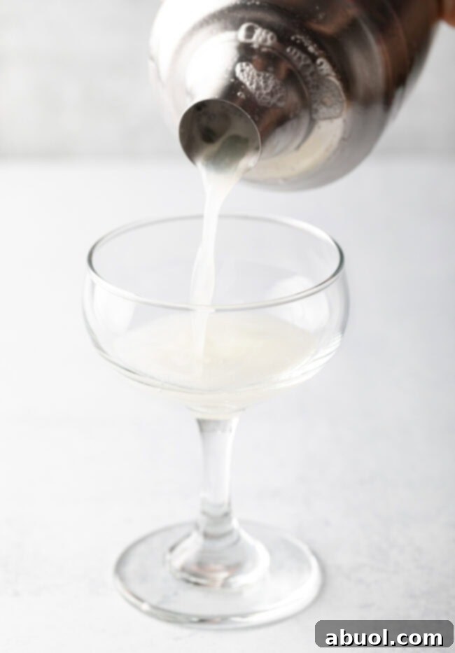 Metal shaker glass pouring clear liquid into a martini glass.