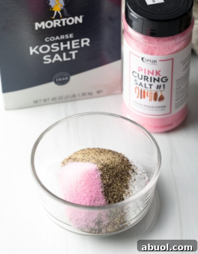Small glass mixing dish with pink curing salt, pepper, and kosher salt.