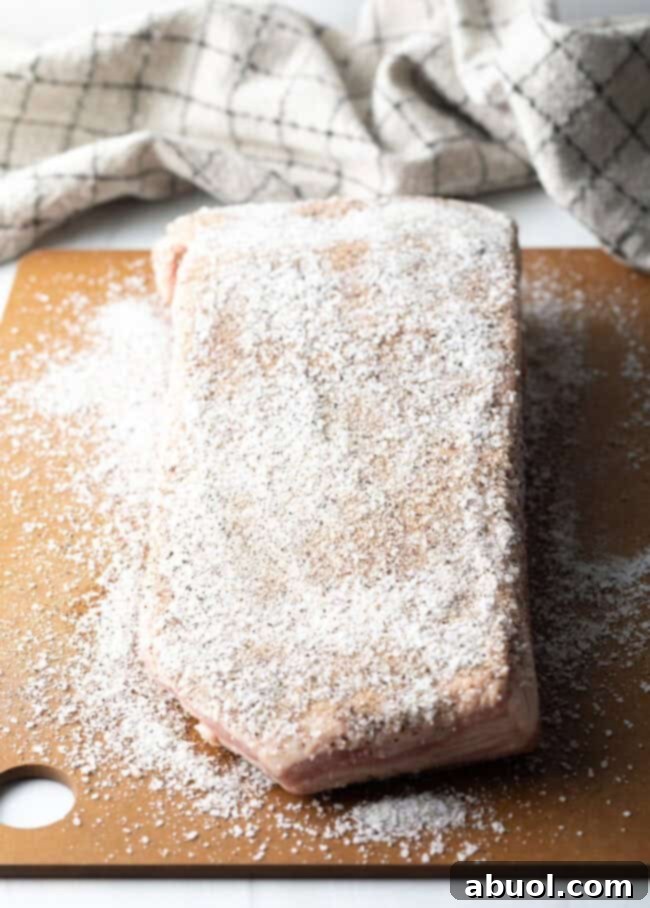 Slab of meat on a cutting board, coated with salt seasoning.