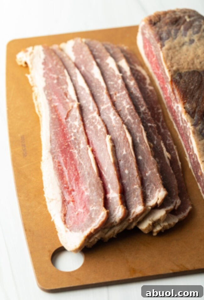 Slab of cured beef bacon cut into 6 thick slices on a cutting board.