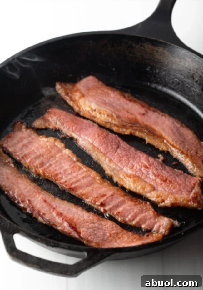 Overhead shot of 4 pieces of beef bacon in a cast iron skillet.
