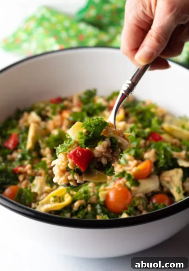 Hand with metal spoon, scooping kale Farro salad from the bowl and holding to camera.