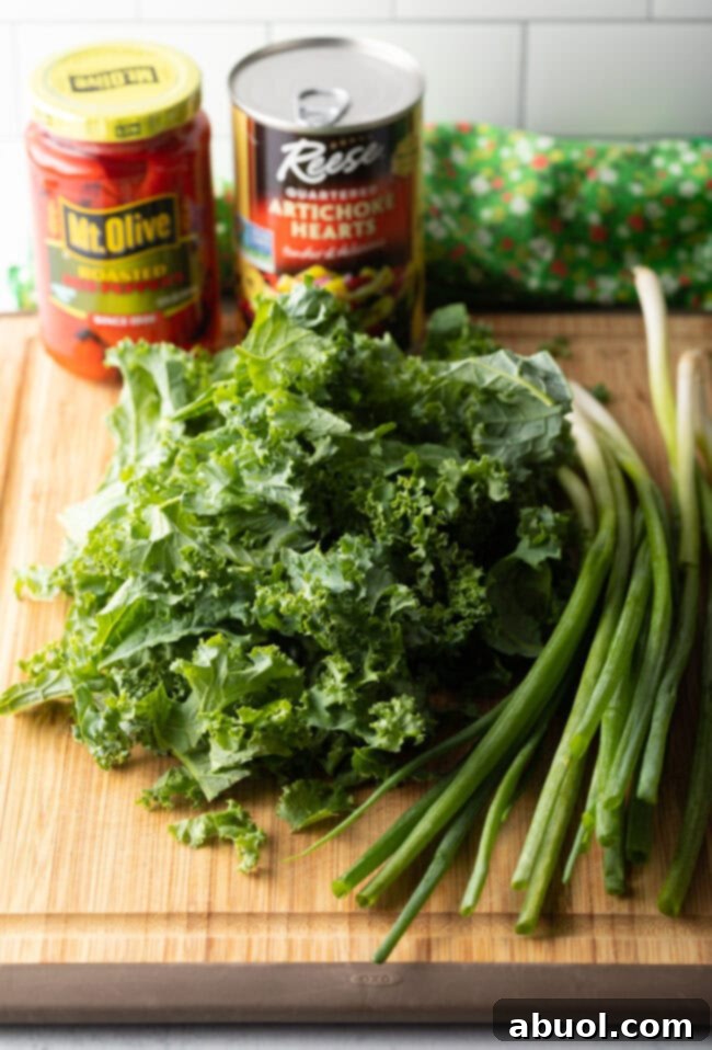 Ingredients on a cutting board: whole kale, green onions, and jarred pepper and artichoke hearts.