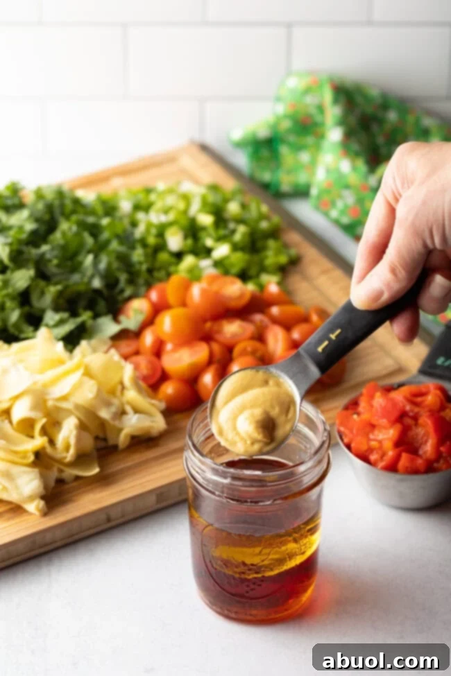 Hand adding 1 tbsp mustard to glass jar with vinaigrette ingredients.