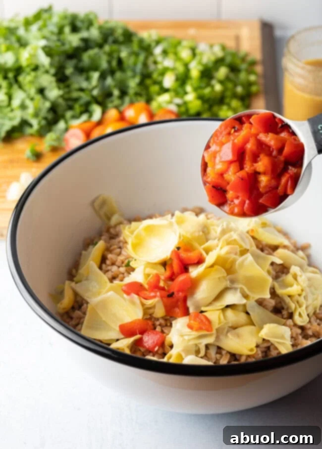 Adding artichoke hearts and chopped red peppers to the bowl with Farro.