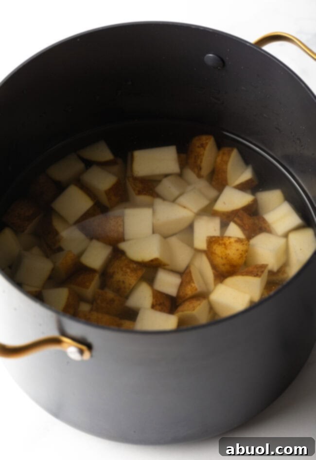 Large black pot with diced potatoes covered in water.