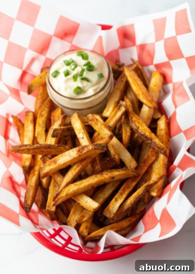 Top down view Cajun french fries in a white and red checkerboard container, with ramekin of dipping sauce.