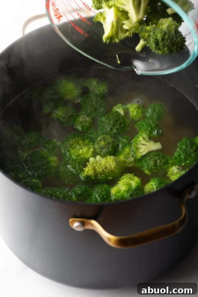 Perfectly Creamy Broccoli Pasta 4 How long to boil broccoli - Fresh florets being poured from glass measuring dish into pot of boiling water.