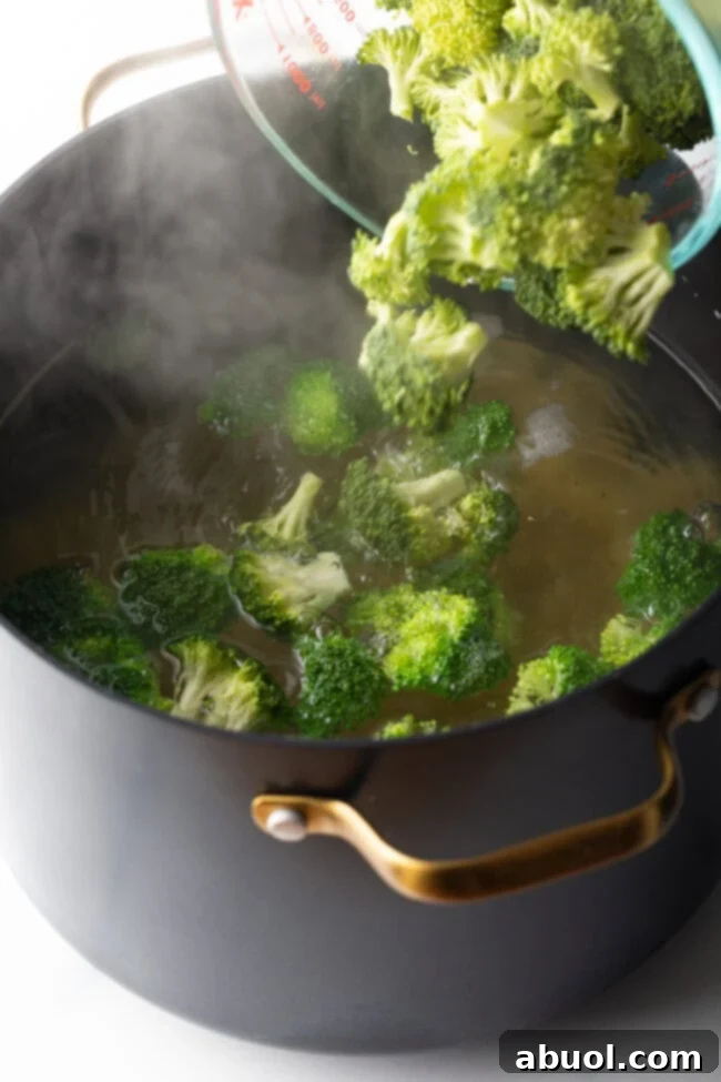 Perfectly Creamy Broccoli Pasta 7 Glass measuring pitcher pouring chopped florets into pot of boiling water.