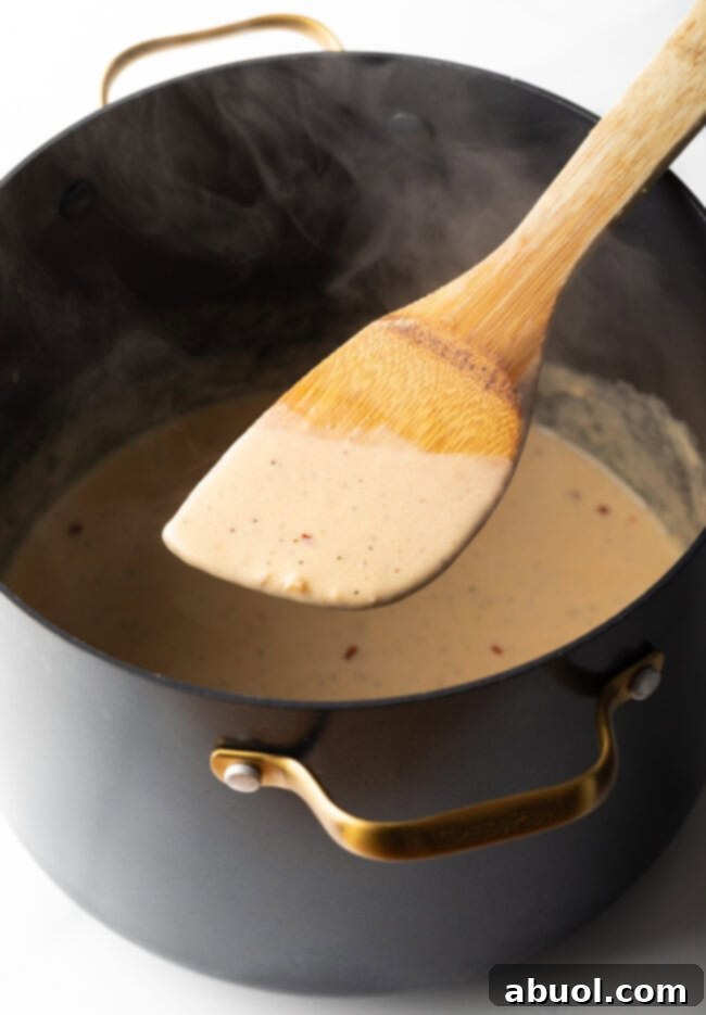Perfectly Creamy Broccoli Pasta 8 Wood spoon showing creamy cheese sauce being made in a large pot to camera.