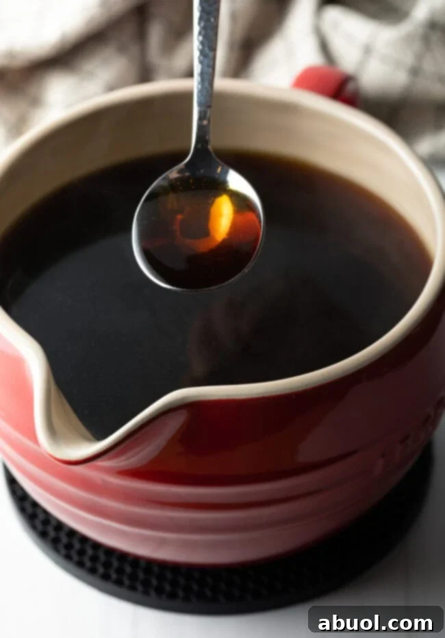 A spoon holding consomme over a ceramic bowl filled with consomme.