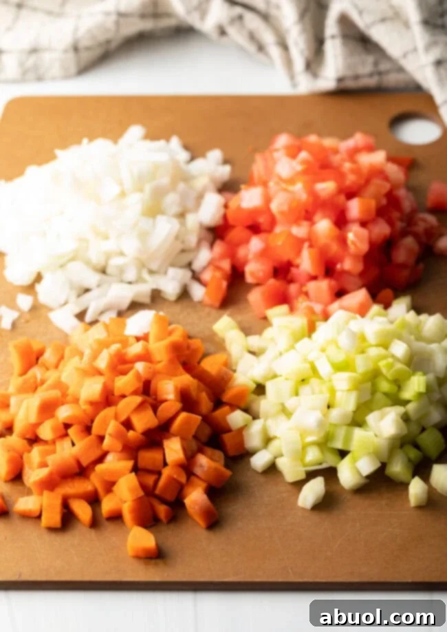 Mirepoux: diced tomatoes, white onion, celery, and carrots on a cutting board.