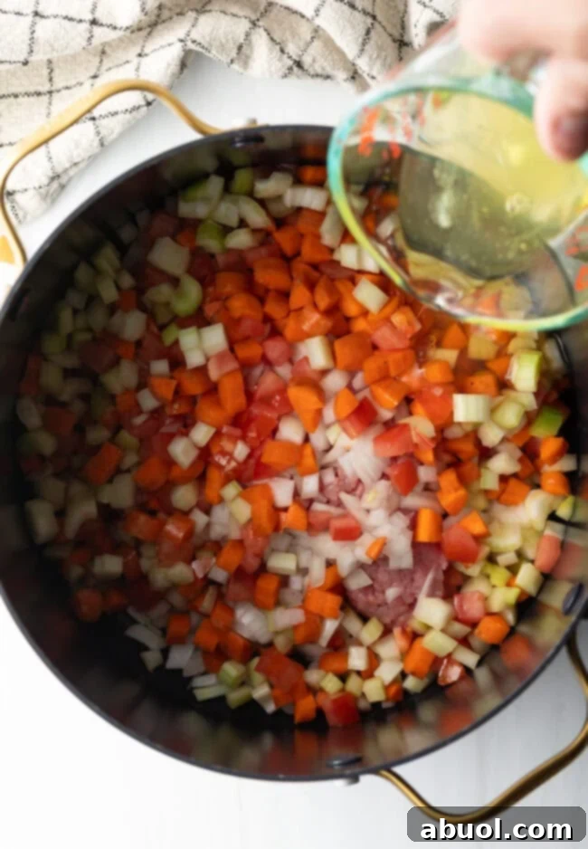 Top down view of consomme ingredients in a pot. A hand is holding a glass measuring cup pouring in egg whites.